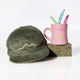 Three items from the 2025 Sundance Fest merch collection: a gray corduroy hat, a pink mug, and multicolored pens inside the mug.
