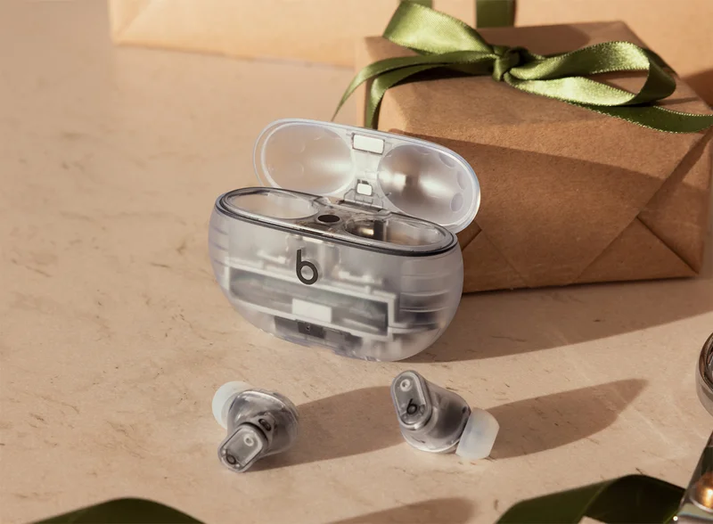Transparent Beats Studio Buds + earbuds with charging case next to a wrapped gift..