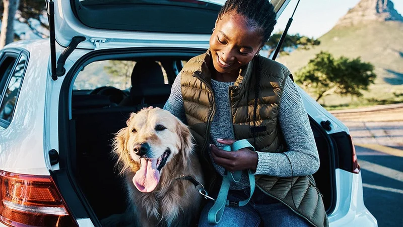 Image description: Woman sitting with dog in the back of an open hatchback of car