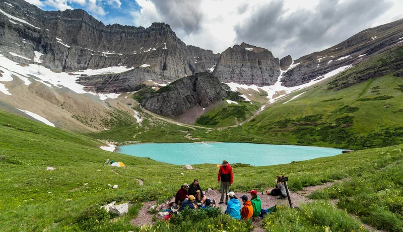 Hikers pause for a break by a crystal blue lake surrounded by mountains