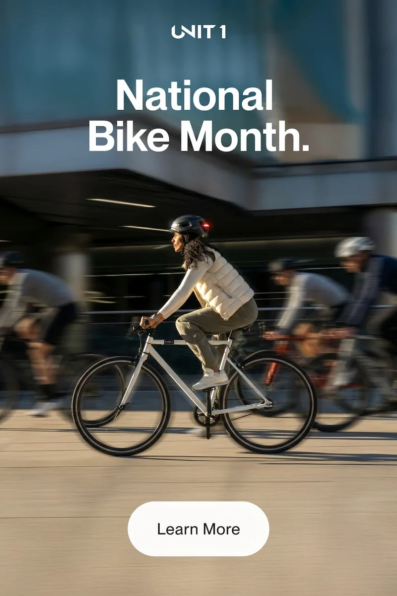 UNIT 1 National Bike Month. Cyclist wearing a lit helmet rides through city traffic