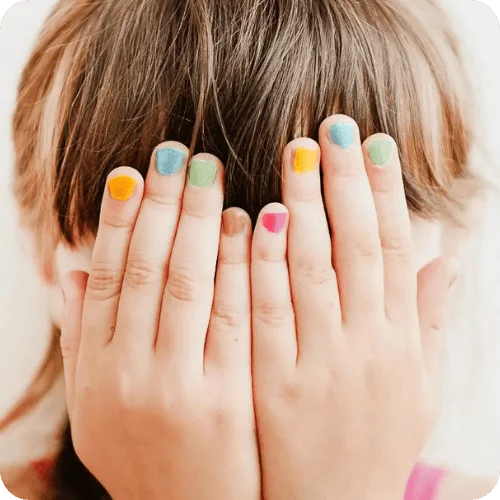 a kid covering their face with their hands that have multicolored nail polish a kid covering their face with their hands that have multicolored nail polish
