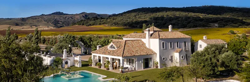 Large villa-style home with a pool, surrounded by open fields and rolling hills.