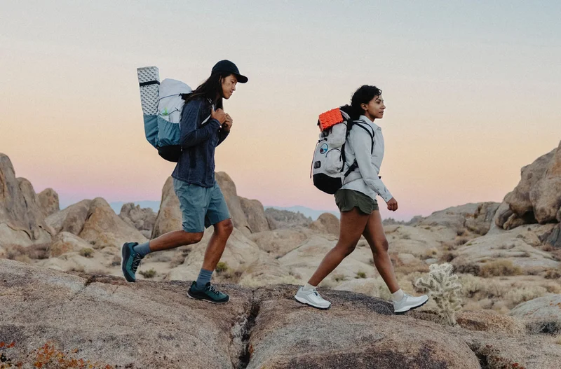 Two people wearing Danner N45 hikers traverse rocky desert terrain at sunset.