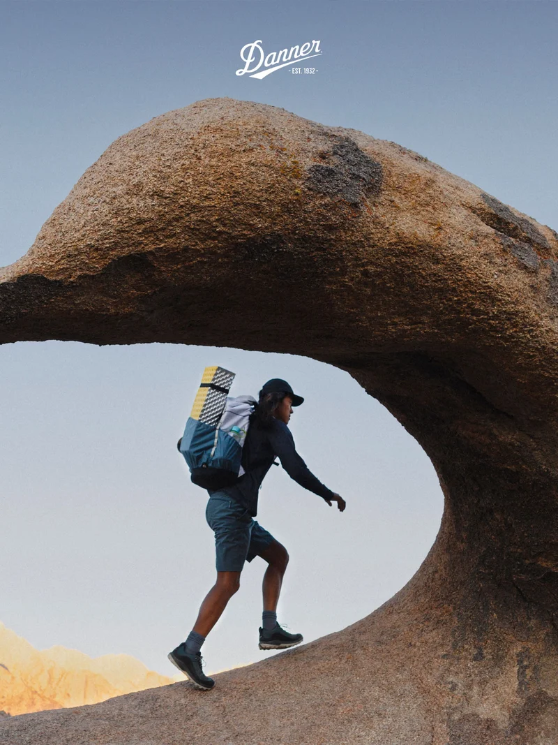 A person wearing a pair of Danner N45 hikers steps through a natural rock arch in a desert landscape.