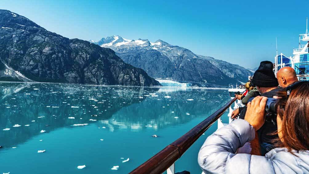 Image description: A tourist filled boat deck in the bay with glacier on a sunny clear sky day.