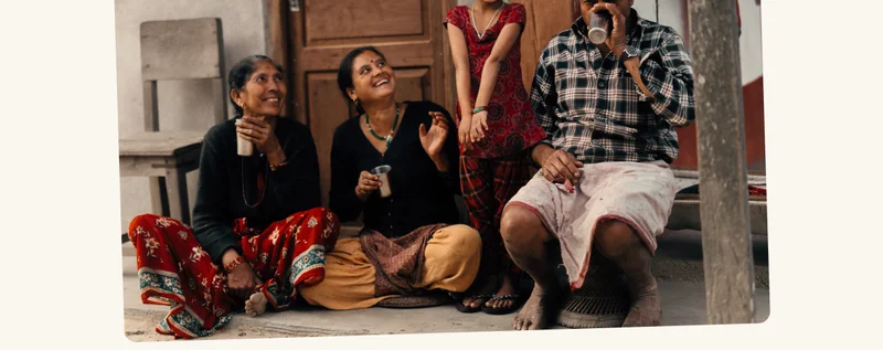 A family in India laugh together outside of their home while drinking clean water.