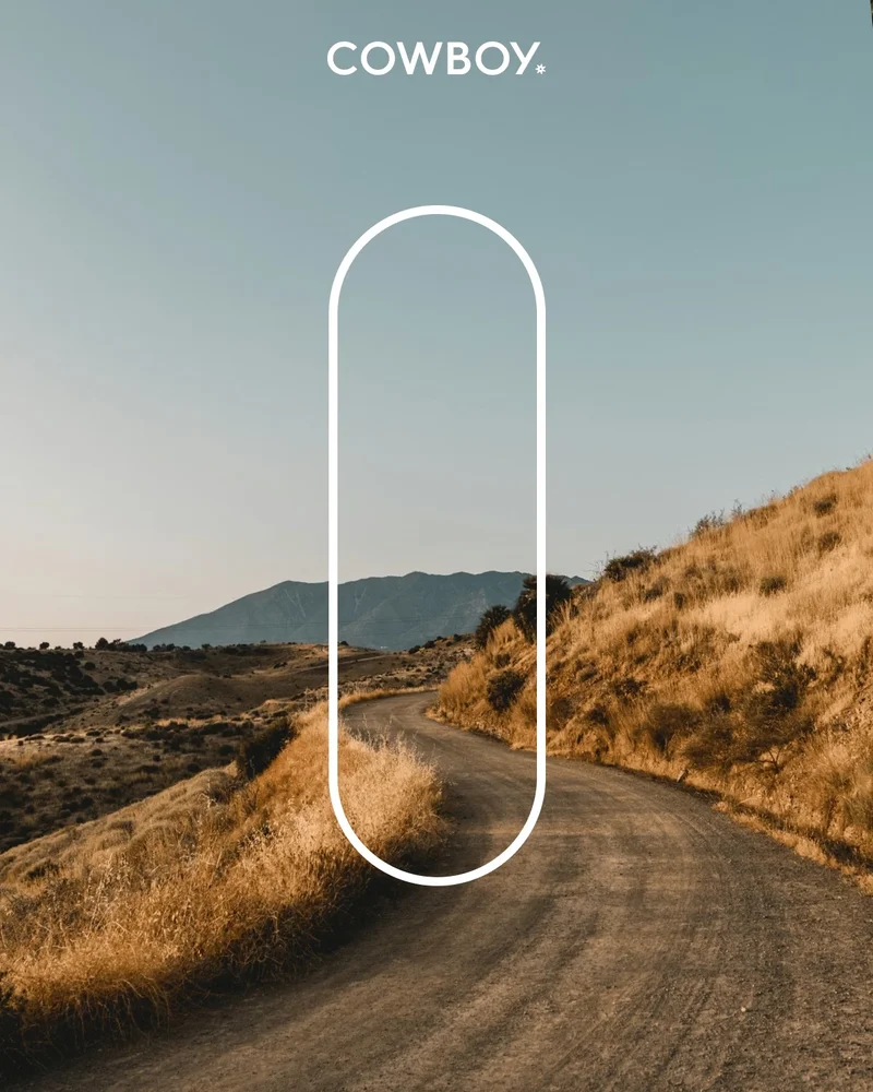 A photographic composition. A road winds past a wild scrubby hill under a deep blue sky. The Cowboy logo is positioned at the top of the image. An outline of a vertical lozenge shape focusses attention on the road.