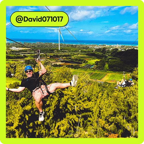 Image description: Man with a helmet hanging on a zipline over a jungle, photo taken by @David071017