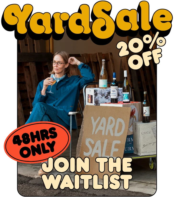 Kirby sitting at our Yard Sale set up with a glass of wine and cardboard sign.