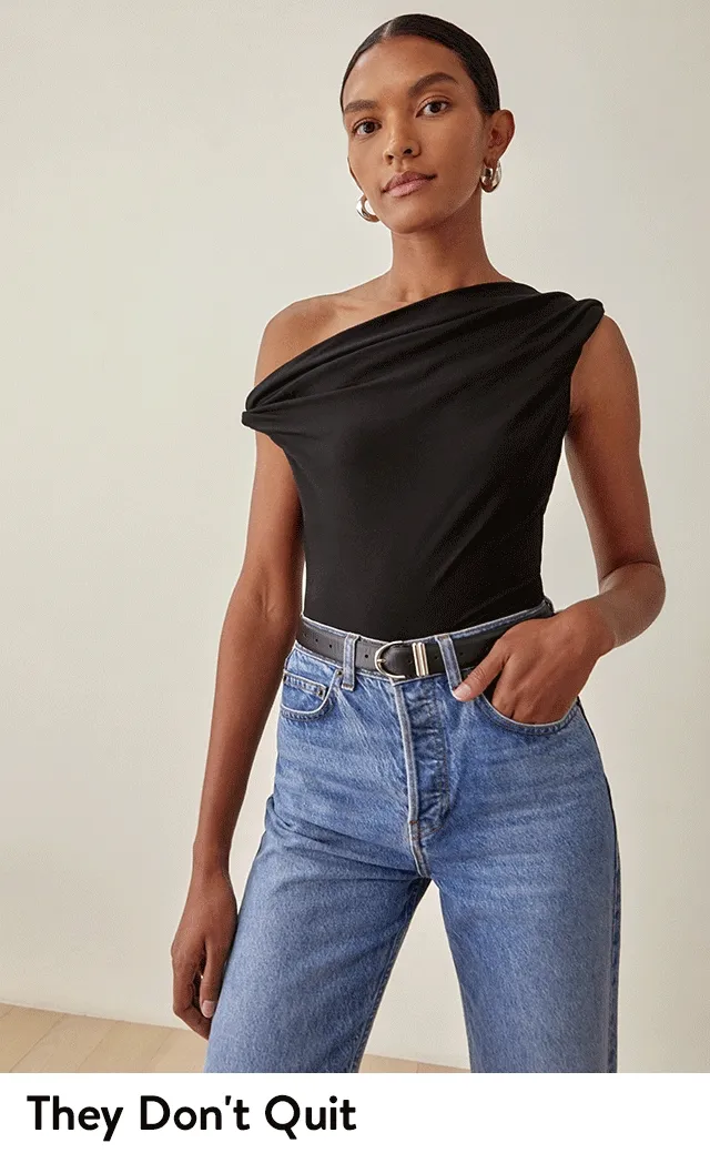 A woman wearing a black one-shoulder top and jeans.