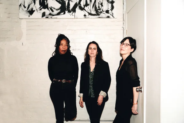 Three jazz musicians standing against a white brick wall