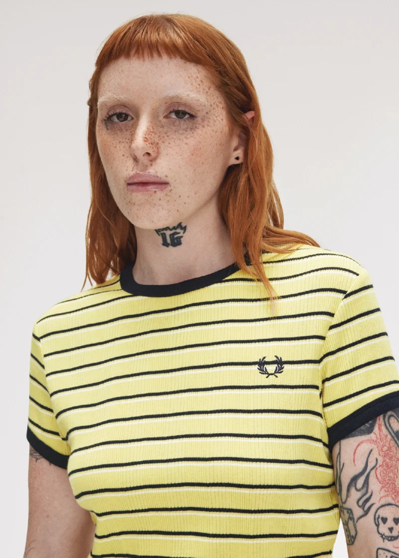 White female model with accentuated freckles and ginger hair with a short fringe wears a pale yellow T-shirt with black stripes and short sleeves