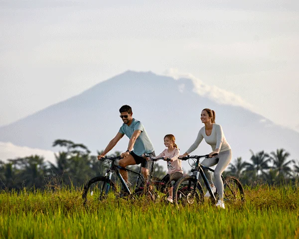 A family of three is bicycling through a grassy field.
