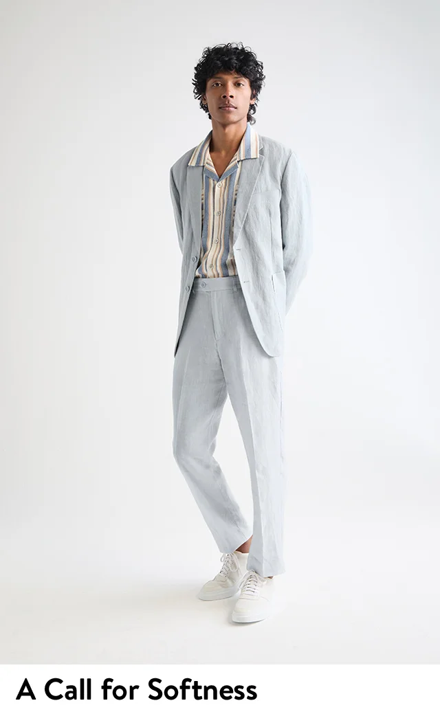 A man wearing a light blue linen suits from Percival and ivory Cole Haan sneakers.