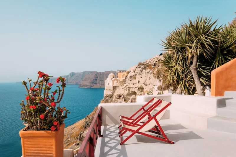 Two lounge chairs sit on a terrace, overlooking the ocean.