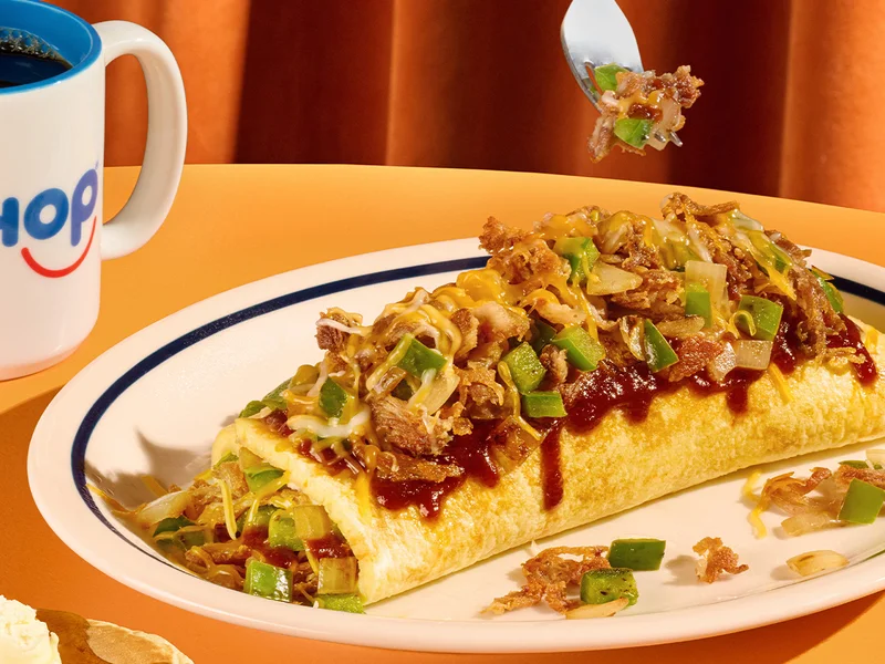The Bold BBQ Pulled Pork Omelette is on a plate, with a fork holding a small bit of pulled pork.