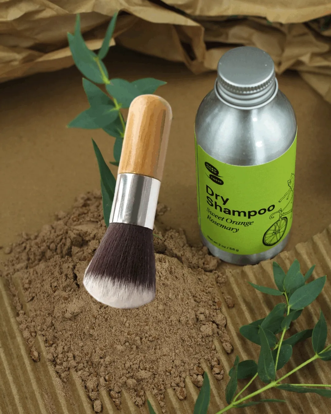 A metal bottle sits on a brown surface with brown powder and a brush wiggles over top