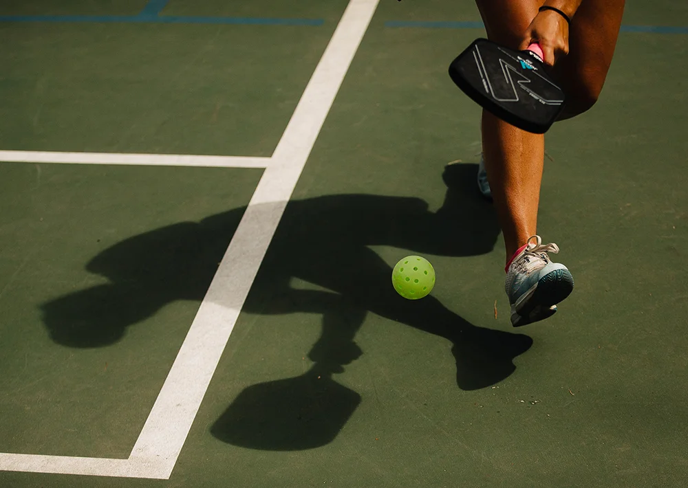 The shadow and legs of a pickelballer chasing down a ball during a match