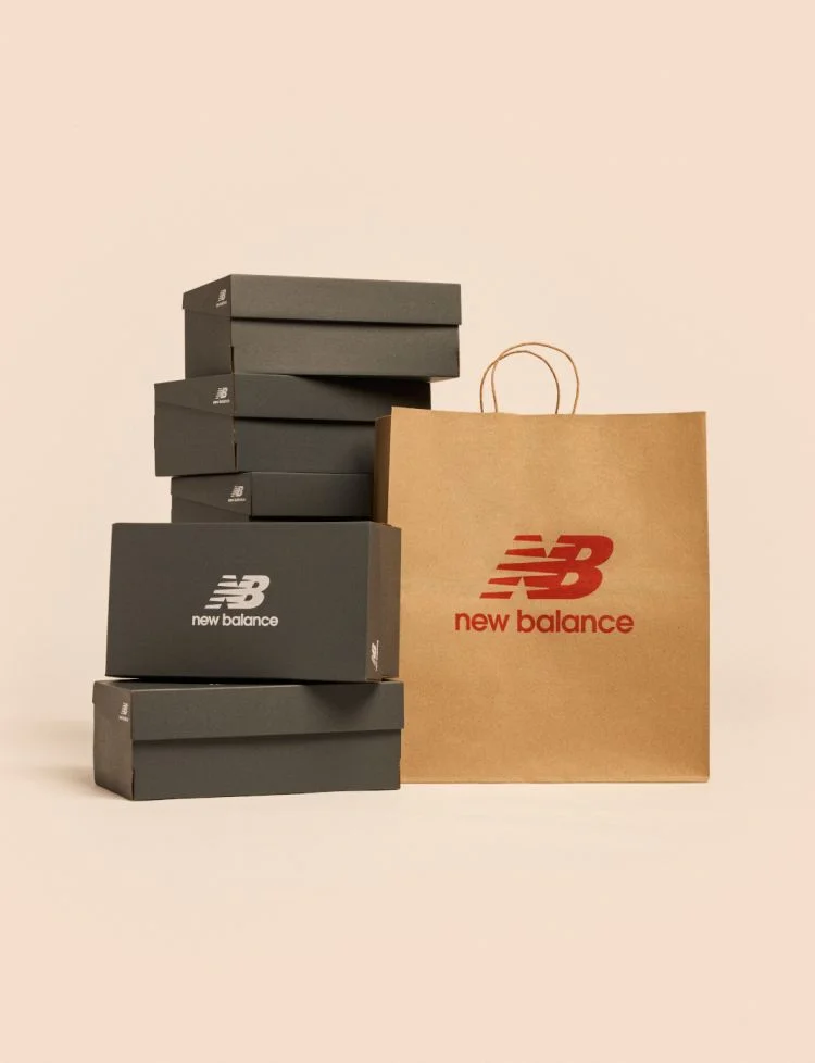 A stack of New Balance shoe boxes next to a shopping bag against a pale apricot backdrop