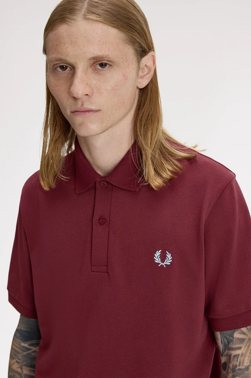 Deep red Fred Perry polo shirt with an ice blue laurel wreath embroidered at the left-side chest