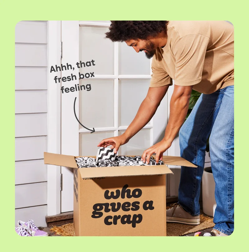 Image: Person unboxing a “Who Gives A Crap” delivery box, with an arrow pointing to text that says “Ahhh, that fresh box feeling”