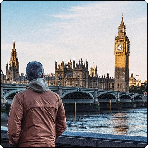 Image Description: A man walking along a river with a bridge and iconic London attractions in the background.