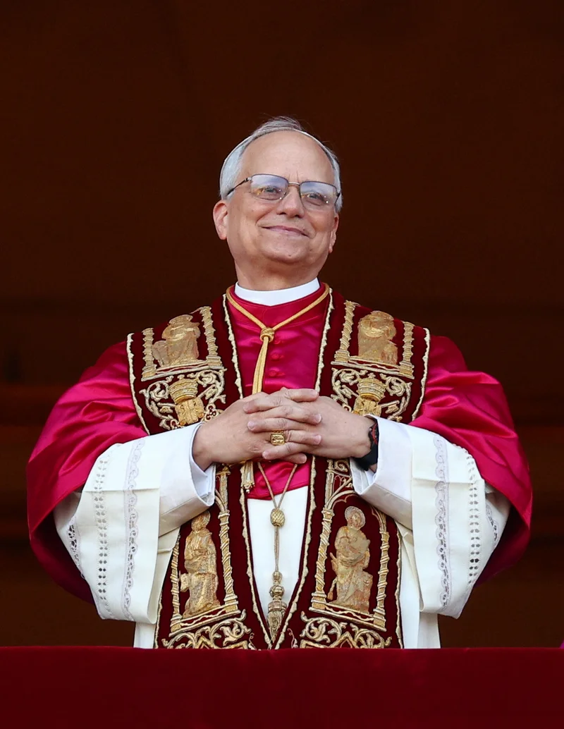 Cardinal Robert Francis Prevost folds his hands and smiles softly. He wears a red and white robe.