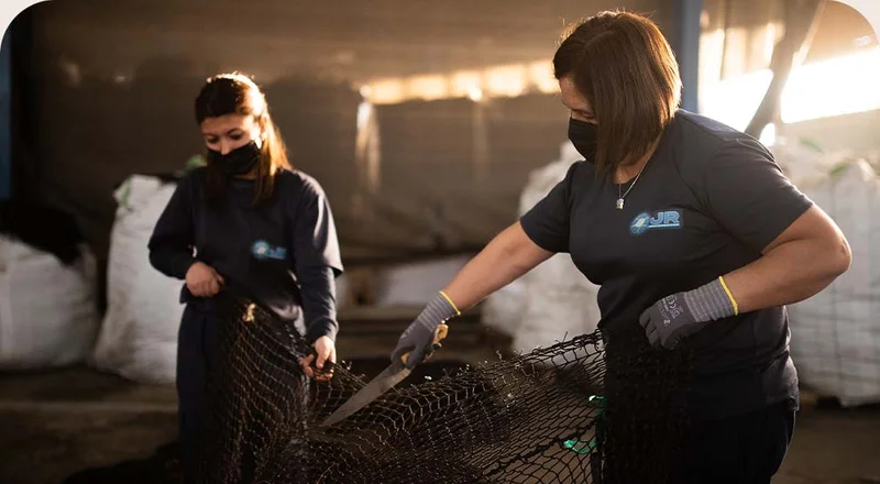 Two people cutting old fishing nets with knives.
