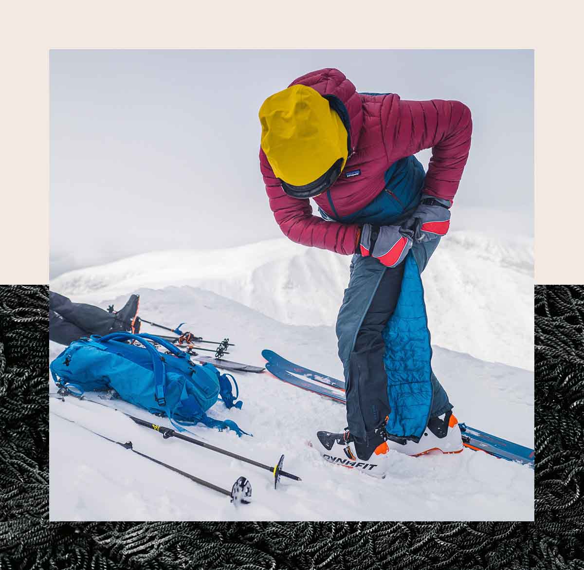 A skier zipping off insulated pants with their skis and poles on the snow.
