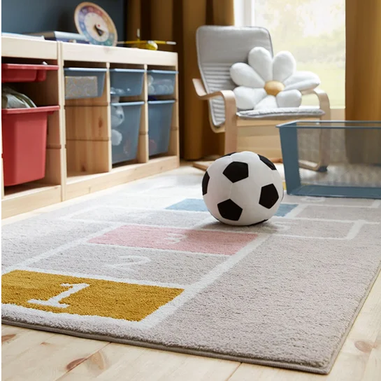 A STÄPPSPARV rug featuring a hopscotch pattern placed in a children’s room with a textile soccer ball and mesh storage units.