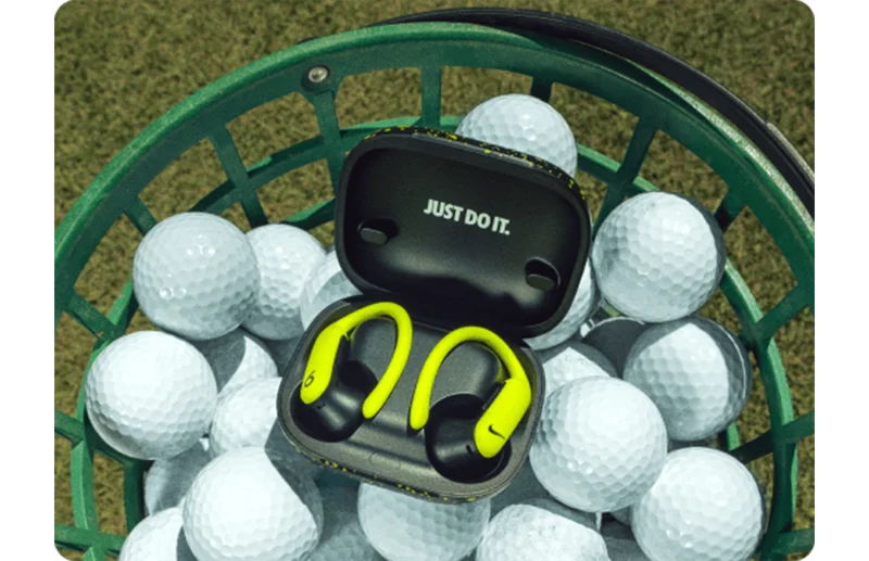 A pair of special-edition Nike Powerbeats Pro 2 earbuds and charging case in a bucket of golf balls.