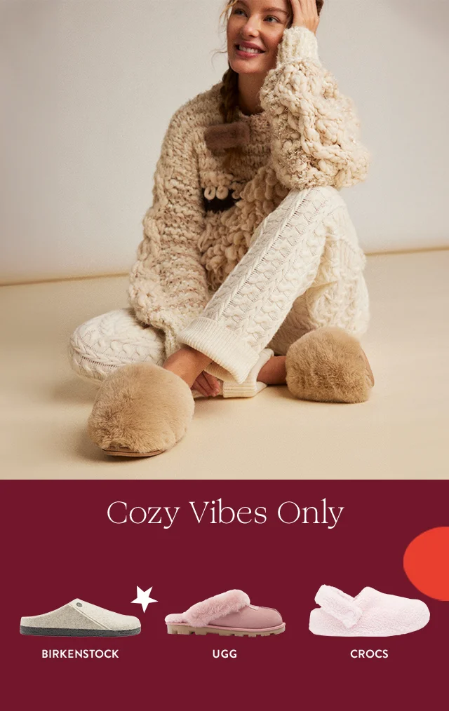 A woman wearing fuzzy brown slippers. Pink Birkenstock clogs, white and grey UGG slides and pink CROCS.