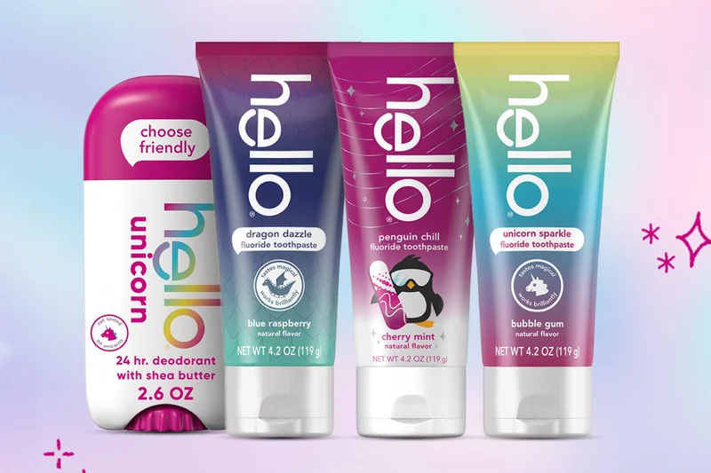 Four Hello Kids products on a pink and blue sparkly background. From left to right: Hello Kids Unicorn Deodorant, Hello Kids Dragon Dazzle Blue Raspberry Fluoride Toothpaste, Hello Kids Cherry Mint Penguin Chill Fluoride Toothpaste, and Hello Kids Unicorn Sparkle Bubble Gum Fluoride Toothpaste.