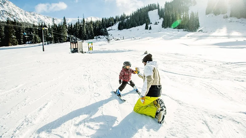 Image description: Father giving high five to toddler after ski lesson at resort