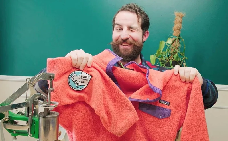 A person winks while holding up a fleece they repaired.