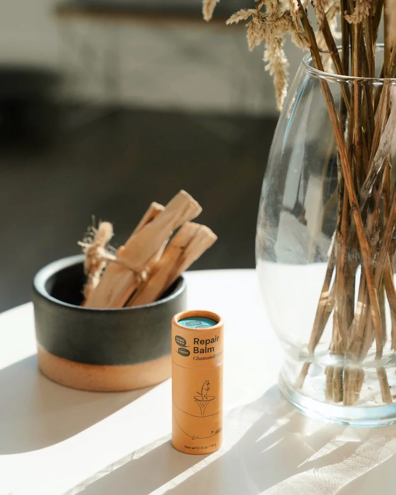 A tan tube sits on a small table with incense and dried flowers