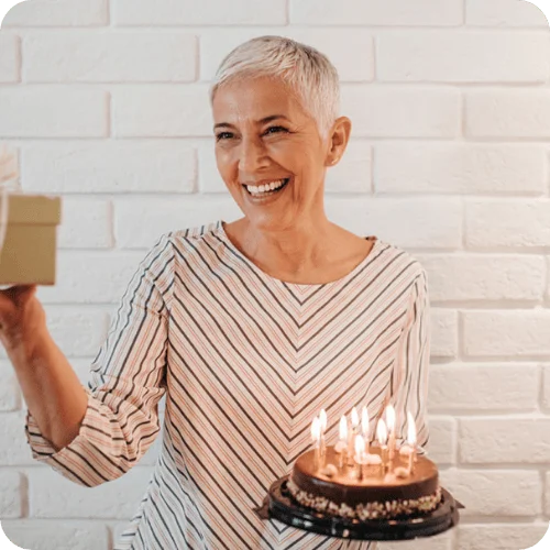 an older woman holding a cake and gift at her grandma shower an older woman holding a cake and gift at her grandma shower