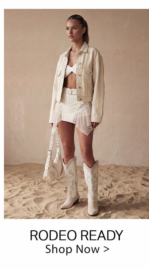 Cream denim jacket, white ruffled mini skirt, and embroidered cowboy boots worn by a model. Explore our 'Rodeo Ready' western wear collection.