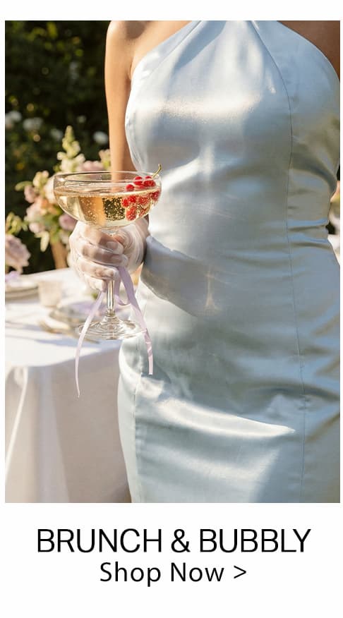 Person in an elegant pale blue satin dress, holding a glass of bubbly with red currants. Shop our Brunch & Bubbly collection now!