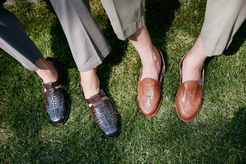 two pairs of mens feet wearing huaraches while standing on grass