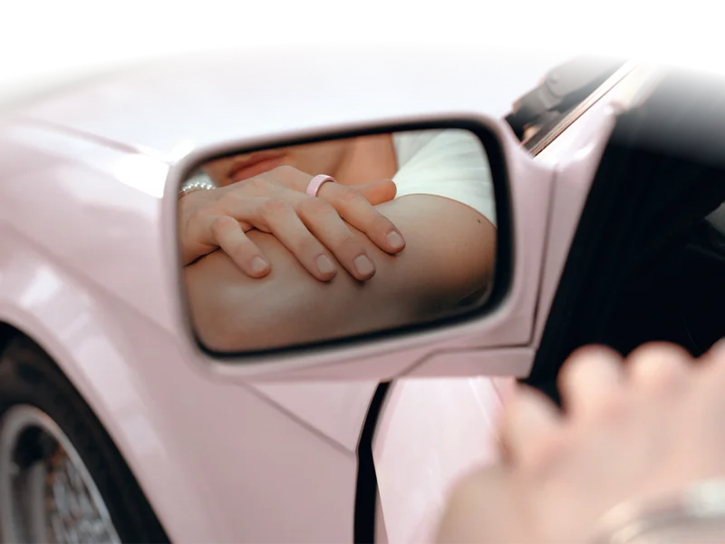 Person wearing Oura Ring 4 Ceramic Petal reflected in pink car side mirror