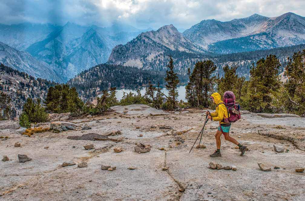 A hiker walks a trail high in the mountains with a storm brewing in the sky.