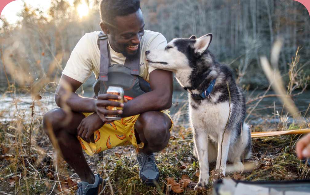 Patagonia Stories. A man wearing a life jacket smiles as he kneels beside and a husky resting its snout against his arm.