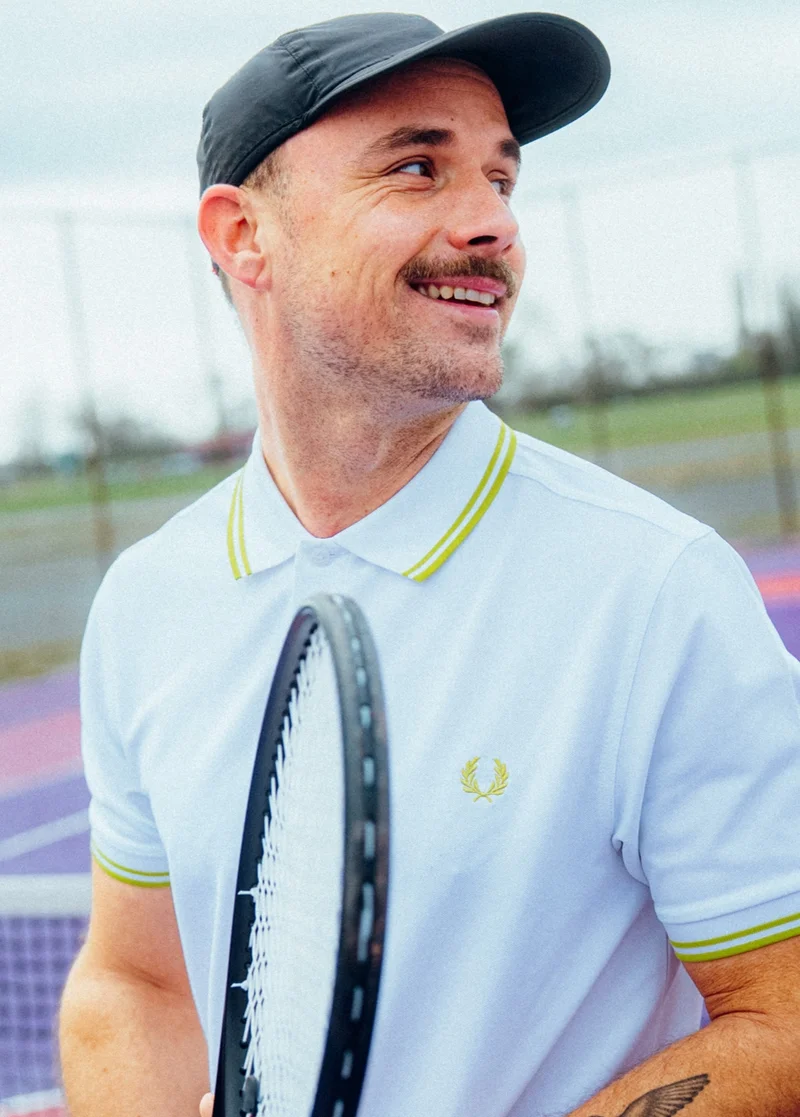 Male wearing a Tennis Fred Perry Shirt in White / Citron / Citron holding a tennis racket
