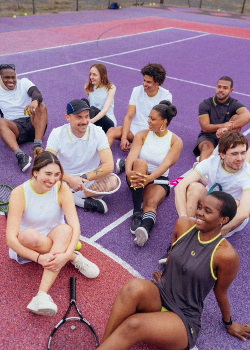 A group of people sitting on a tennis court wearing Fred Perry Tennis