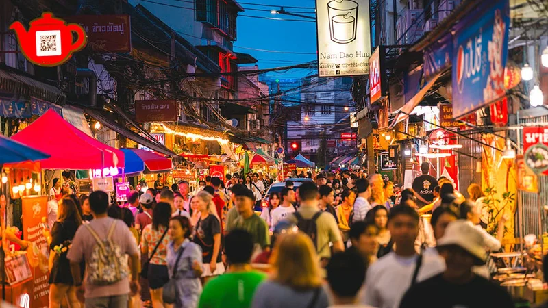 Image description: Crowd of people walking through a night market in Bangkok, Thailand.