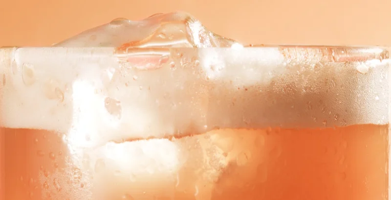 Close-up of iced chai beverage in a glass with froth and condensation.