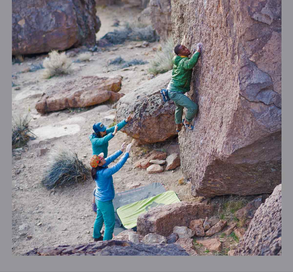 New Arrivals. A climber scales a bouldering problem while two people spot him below.