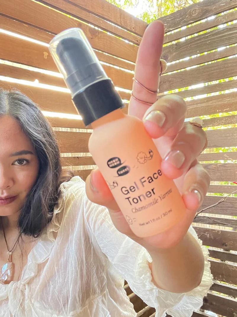 A tan-skinned person holding a pink bottle in front of the camera